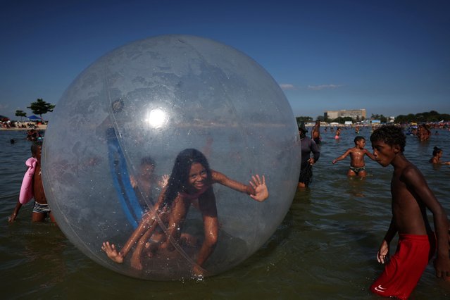 A girl tries to balance inside a ball at the artificial pond known as Piscinao de Ramos, or big pool, during a heatwave in the northern suburbs of Rio de Janeiro, Brazil, on February 16, 2025. (Photo by Pilar Olivares/Reuters)