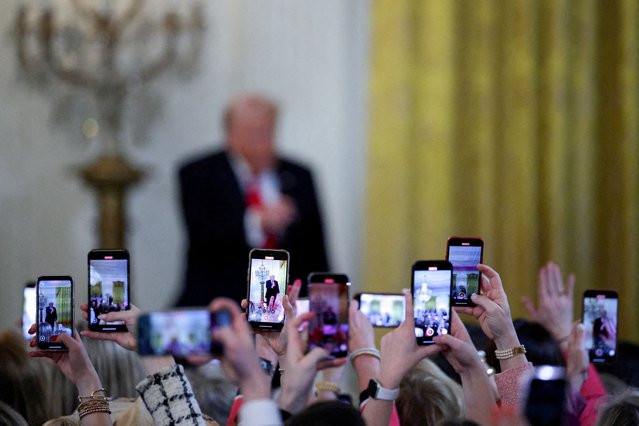 Attendees record as U.S. President Donald Trump speaks during a Women's History Month event at the White House on March 26, 2025. (Photo by Carlos Barria/Reuters)