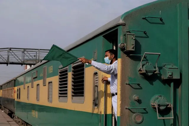 A railway staff member wearing a protective mask, waves green signal flag as train leaves at the Cantonment railway station, as the outbreak of the coronavirus disease (COVID-19) continues, in Karachi, Pakistan on July 8, 2020. (Photo by Akhtar Soomro/Reuters)