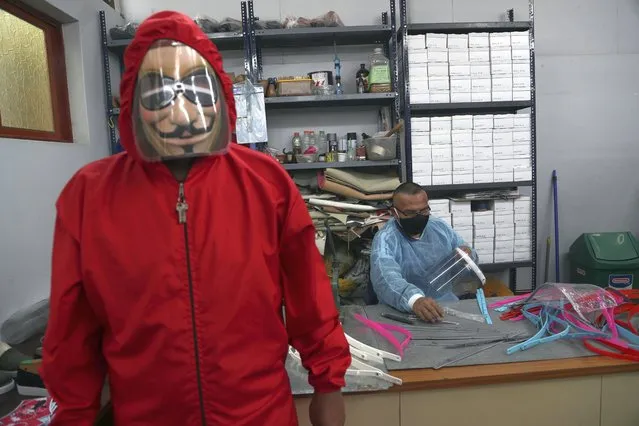 An inmate models the protective gear inmates manufacture as fellow inmate Luis Huaman makes face shields at a workshop in the Lurigancho prison, on the outskirts of Lima, Peru, Wednesday, August 19, 2020. Health authorities and inmates look to implement protocols to curb the spread of COVID-19 at the overcrowded prison. (Photo by Martin Mejia/AP Photo)