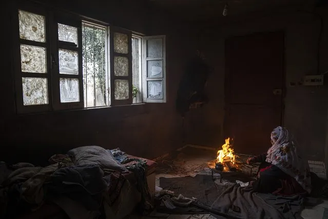 A Palestinian woman warms herself by a fire during a cold weather in Dier al-Balah, central Gaza Strip Monday, December 26, 2022. (Photo by Fatima Shbair/AP Photo)