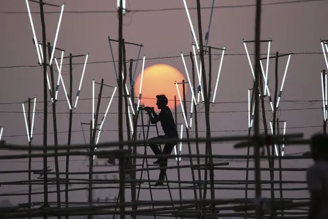 A worker installs lights at an outdoor location of a film shoot in Bhopal on January 13, 2023. (Photo by Gagan Nayar/AFP Photo)
