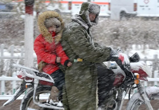 A motorcyclist and child ride against wind in snow in Balikun, Xinjiang Uighur Autonomous Region, November 25, 2014. Picture taken November 25, 2014. (Photo by Reuters/China Daily)