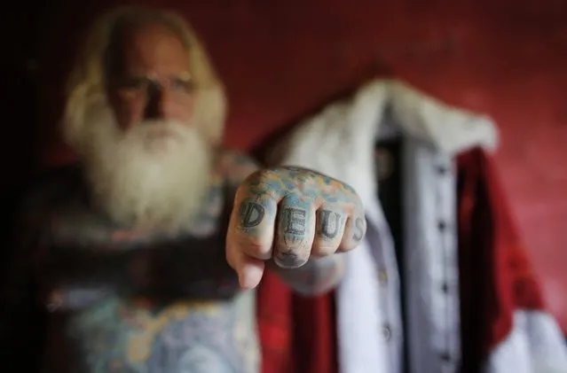 Vitor Martins puts forward his fist, that has the word “God” tattooed on it, in front of his Santa Claus outfit inside his house, before a performance with children in Sao Caetano do Sul's town square, near Sao Paulo, December 7, 2014. Martins has dressed as Santa Claus, working at shopping centres and various events, for fifteen years, and has 94 percent of his body covered in tattoos, with several in reference to Christmas. (Photo by Nacho Doce/Reuters)