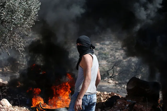 A Palestinian protester stands in front of burning tires during clashes with Israeli security forces following a weekly demonstration against the expropriation of Palestinian land by Israel in the village of Kfar Qaddum, near Nablus in the occupied West Bank, on October 7, 2016. (Photo by Jaafar Ashtiyeh/AFP Photo)