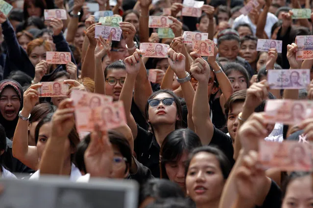 People display portraits of Thailand's King Bhumibol Adulyadej on Thai baht notes as they wait on the roadside while his body is being moved from the Bangkok hospital where he died to the Grand Palace, in Bangkok, Thailand, October 14, 2016. (Photo by Chaiwat Subprasom/Reuters)