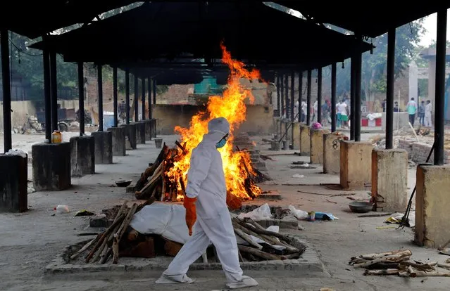 A priest wearing personal protective equipment (PPE) walks in front of the body of a person who died of the coronavirus disease as he collects woods to make a funeral pyre at a crematorium in New Delhi, India, July 3, 2020. (Photo by Anushree Fadnavis/Reuters)