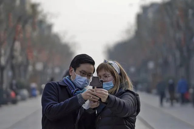Visitors wearing face masks to help curb the spread of the coronavirus take a smartphone photo of an ice-cream with a shaped of Qianmen Gate which bought at Qianmen Street, a popular tourist spot in Beijing, Sunday, January 31, 2021. A World Health Organization team looking into the origins of the coronavirus pandemic on Sunday visited the seafood market in the Chinese city of Wuhan that was linked to many early infections. (Photo by Andy WongAP Photo)