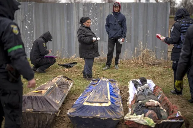 Valya Naumenko, 47, identifies the body of her husband Pavlo Ivanyuk, 57, killed by Russian Army, during an exhumation of four civilians killed and buried in a mass grave in Mykulychi, Ukraine on Sunday, April 17, 2022. All four bodies in the village grave were killed on the same street, on the same day. Their temporary caskets were together in a grave. On Sunday, two weeks after the soldiers disappeared, volunteers dug them up one by one to be taken to a morgue for investigation. (Photo by Emilio Morenatti/AP Photo)