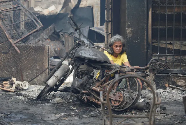 A fire victim sits next to a burnt motorcycle after a fire in the residential district of Addition Hills in Mandaluyong, Metro Manila, Philippines, November 14, 2016. (Photo by Erik De Castro/Reuters)
