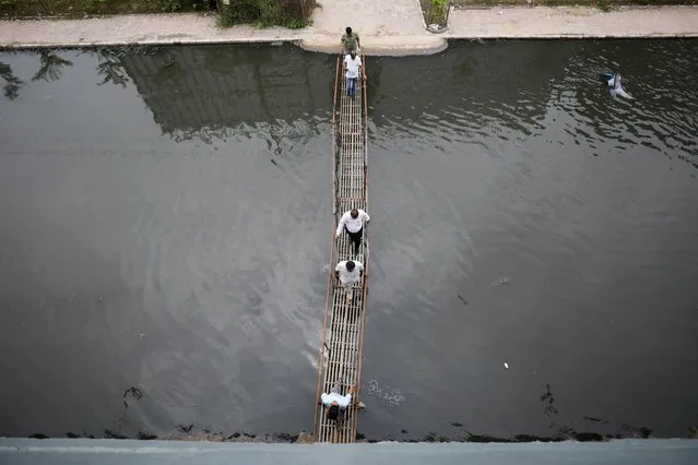 People walk through a makeshift bridge above the waterlogged street after a heavy rain in Ahmedabad, India on July 12, 2023. (Photo by Amit Dave/Reuters)