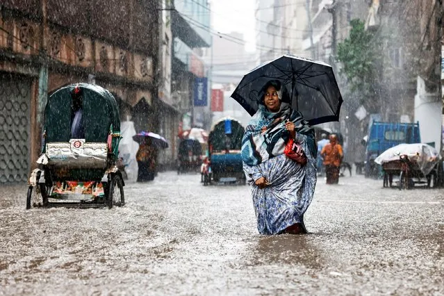 A woman holds an umbrella while walking along a flooded street during heavy rain in Dhaka, Bangladesh on June 12, 2023. (Photo by Mohammad Ponir Hossain/Reuters)