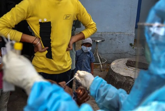 A child wearing a mask as a precaution against the coronavirus watches as a health worker takes a nasal swab sample of a woman to test for COVID-19 at a hospital in Hyderabad, India, Monday, April 19, 2021. (Photo by Mahesh Kumar A./AP Photo)