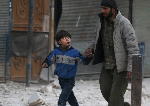 A man holds the hand of a boy as they flee deeper into the remaining rebel-held areas of Aleppo, Syria December 9, 2016. (Photo by Abdalrhman Ismail/Reuters)