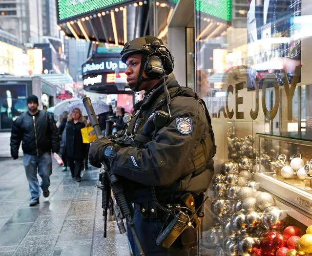 A heavily armed counterterrorism officer takes shelter beneath an overhang above a store in Times Square, Thursday, December 29, 2016, in New York. The city's police are once again saying they are up to the task of protecting the huge crowds that are expected to gather in and around Times Square for New York City's massive New Year's Eve celebration. (Photo by Kathy Willens/AP Photo)