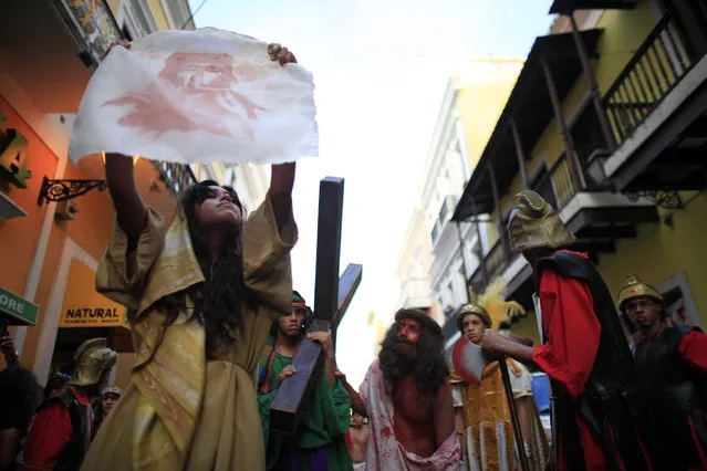 A woman holds up a cloth with an image of Jesus' face in red, believed to be from Jesus' blood after his face was wiped with it, during a reenactment of Jesus' last hours at a Stations of the Cross procession during Holy Week in San Juan, Puerto Rico, on Good Friday, April 3, 2015. Good Friday recalls Jesus' death by crucifixion. (Photo by Ricardo Arduengo/AP Photo)