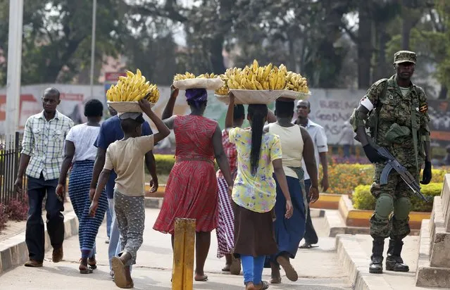 Women carry baskets of banana as they walk past a military personnel patrolling in Uganda's capital Kampala, February 19, 2016. Ugandan police shot in the air and fired tear gas at opposition protesters in several parts of southern Kampala on Friday, a Reuters witness said, after the presidential election a day earlier. (Photo by James Akena/Reuters)