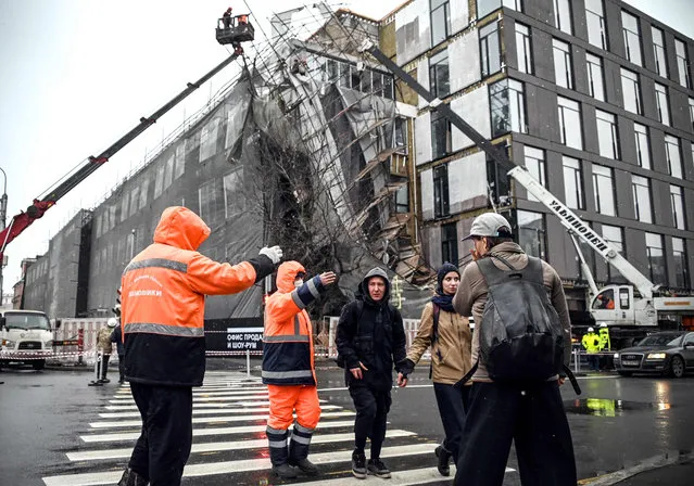 Municipal workers stops people trying to cross a street to a restricted area after scaffolding has collapsed during a storm in Moscow on November 30, 2021. (Photo by Alexander Nemenov/AFP Photo)