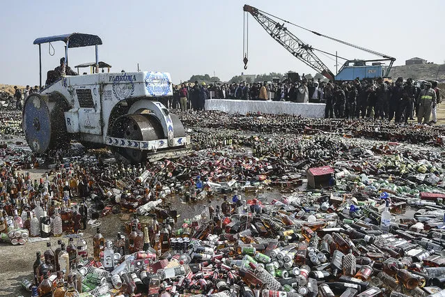 An official uses a steamroller to crush bottles of seized liquor during an event organized to destroy seized illicit alcohol and drugs smuggled into the country, in Karachi on December 29, 2021. (Photo by Rizwan Tabassum/AFP Photo)