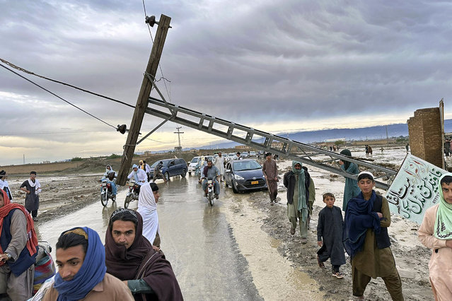 People pass by a damaged electric pole caused by flooding due to heavy rains near Chaman area, Pakistan, Thursday, April 18 2024. Lightning and heavy rains led to 14 deaths in Pakistan, officials said Wednesday, bringing the death toll from four days of extreme weather to at least 63, as the heaviest downpour in decades flooded villages on the country's southwestern coast. Flash floods have also killed dozens of people in neighboring Afghanistan. (Photo by Habib Ullah/AP Photo)