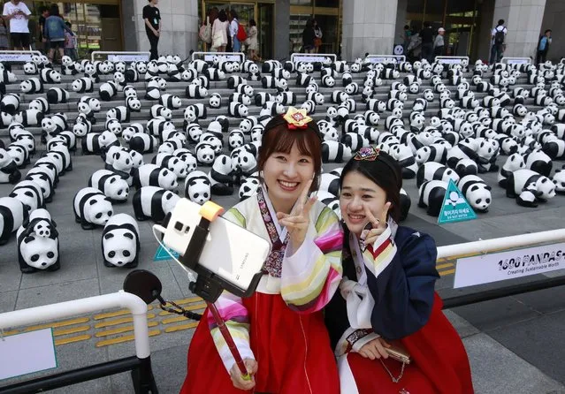 South Korean Chun Un-ji and Jin Soo-jung, right, wearing traditional costumes take a selfie with the some of the 1,600 paper pandas, created by French artist Paulo Grangeon, during the month-long “1,600 Pandas World Tour” in Seoul, South Korea, Saturday, May 23, 2015. (Photo by Ahn Young-joon/AP Photo)