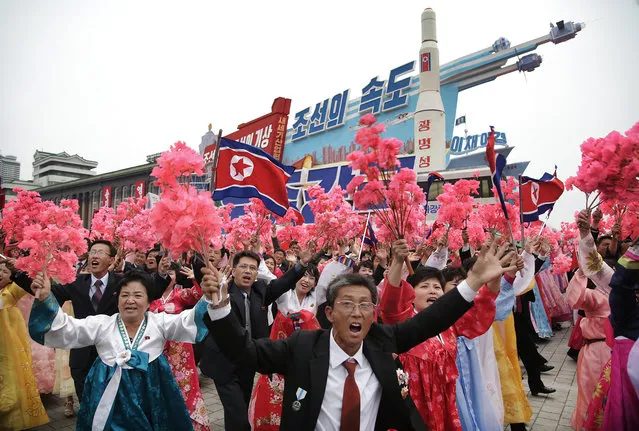 North Korean parade participants wave decorative bouquets of flowers and carry their country's national flag as they march with a model of the Unha space launch vehicle at the Kim Il Sung Square on Tuesday, May 10, 2016, in Pyongyang, North Korea. (Photo by Wong Maye-E/AP Photo)