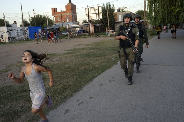 A girl runs as border police agents patrol in Los Pumitas neighborhood, where Maximo Jerez, an 11-year-old boy killed early Sunday when at least one gunmen attacked a birthday party, in Rosario, Argentina, Thursday, March 9, 2023. Hours after Máximo was buried Monday, people in the northern Rosario neighborhood where the alleged shooter lived attacked and wrecked his home. People destroyed at least 3 houses in the area they claimed were used by drug dealers. (Photo by Rodrigo Abd/AP Photo)