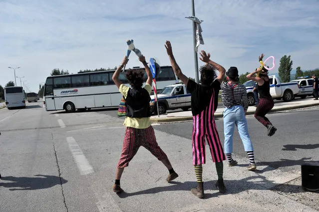 Clowns from a solidarity group wave to  migrants onboard a bus, as they are evacuated from the makeshift camp at the Greek-Macedonian border, near the Greek village of Idomeni, on May 24, 2016. Hundreds of Greek police on May 24 began clearing the overcrowded Idomeni camp, a migrant flashpoint on the Macedonia border where thousands have been living in squalid conditions for more than three months. (Photo by Sakis Mitrolidis/AFP Photo)