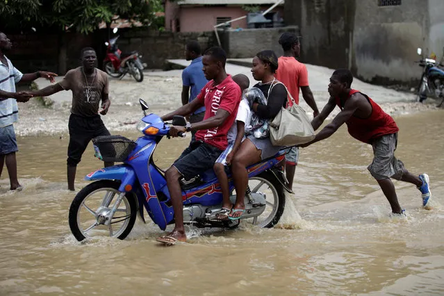 A man pushes a motorbike as it passes a flooded area along National Road #2 in Leogane, Haiti, May 27, 2016. (Photo by Andres Martinez Casares/Reuters)