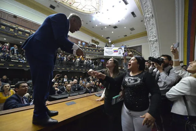 Opposition lawmaker William Barrientos stands on a desk to argue with ruling party lawmakers after many of his allies, including Assembly President Juan Guaidó, were blocked by police from entering the session to elect new leadership in Caracas, Venezuela, Sunday, January 5, 2020. Without a quorum, there was no vote for ruling party Luis Parra, who swore himself in as president of the legislature, while the opposition, who enjoy a comfortable majority, immediately denounced the impromptu session as invalid. (Photo by Matias Delacroix/AP Photo)