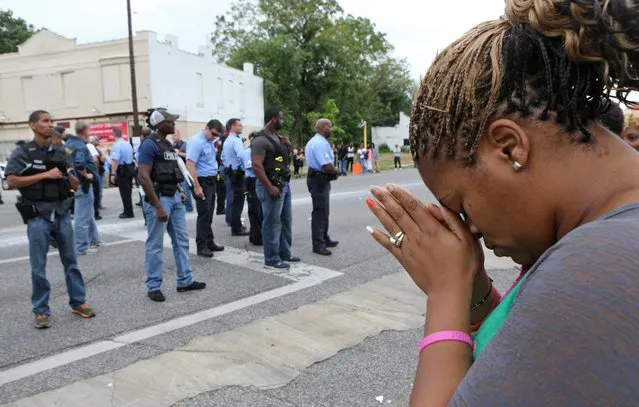 Rhonda Tunstall, 40, prays for peace in the middle of the street as police move in to disperse the large crowd gathered at Page and Walton, Wednesday, August 19, 2015 in St. Louis. An armed man fleeing from officers serving a search warrant at a home in a crime-troubled section of north St. Louis was shot and killed Wednesday by police after he pointed a gun at them, the police chief said. (Photo by David Carson/St. Louis Post-ispatch via AP Photo)