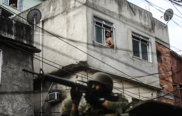 A man watches from a window as a Brazilian soldier aims his weapon while on patrol in the Rocinha 'favela' community on September 24, 2017 in Rio de Janeiro, Brazil. The Brazilian Army and other armed forces entered the favela September 22 in an ongoing operation following firefights involving drug gangs in the favela, which is one of the largest in Latin America. (Photo by Mario Tama/Getty Images)