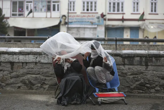 Laborers cover themself with a plastic sheet in the rain as they wait for customers in Kabul, Afghanistan, Monday, April 6, 2020. (Photo by Rahmat Gul/AP Photo)