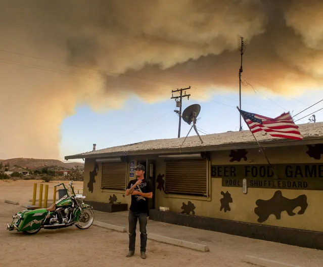 Trevor Rainwater watches a wildfire burn into Summit Valley from the Joshua Inn which was evacuated moments later Sunday, August 7, 2016, in Hesperia Calif. Firefighters are battling a wildfire in Southern California that grew to more than 2 square miles in mere hours and forced the evacuation of homes near a reservoir. The fire, which broke out Sunday afternoon in the San Bernardino National Forest, prompted the evacuation order of the sparsely populated Summit Valley area east of the dam. (Photo by James Quigg/The Daily Press via AP Photo)