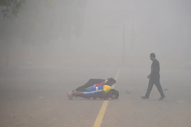 Indian fitness enthusiasts work out amid heavy smog near India Gate in New Delhi on November 13, 2017. Schools reopened in New Delhi on November 13 despite a fresh spike in pollution to emergency levels, drawing protests from parents in the Indian capital who said the move put children's health in jeopardy. (Photo by Dominique Faget/AFP Photo)