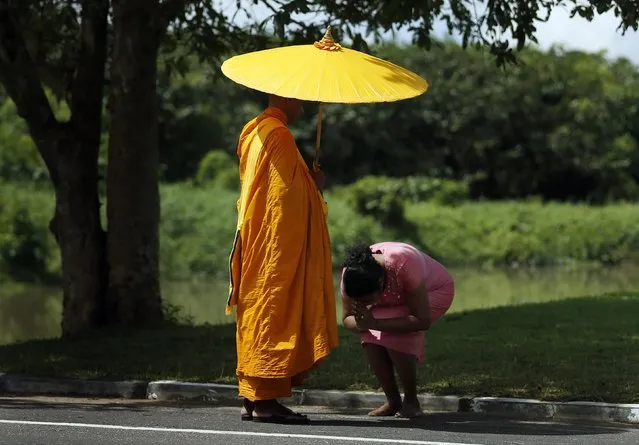 A woman bows in respect to a Buddhist monk after offering alms to him on a main road in Colombo October 17, 2014. (Photo by Dinuka Liyanawatte/Reuters)