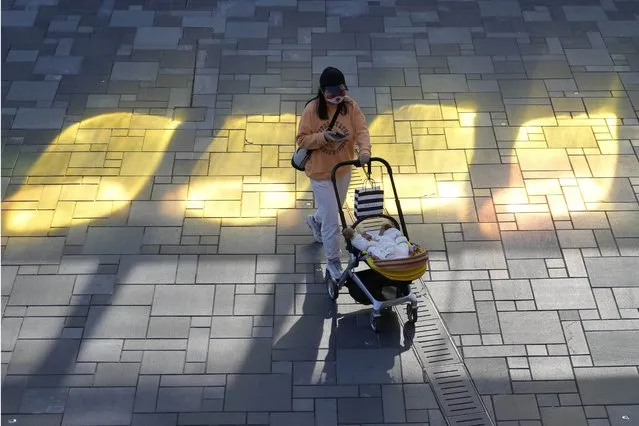 A woman wearing mask pushes a child in pram as she visits a shopping district in Beijing, Tuesday, November 15, 2022. (Photo by Ng Han Guan/AP Photo)