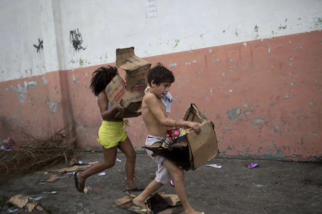 Children run off with boxes they filled with merchandise salvaged from a cargo truck allegedly set on fire by drug traffickers in Rio de Janeiro, Brazil, Tuesday, May 2, 2017. Several public buses and cargo trucks were torched in what military police said was likely gang retaliation for a large anti-drug operation. (Photo by Silvia Izquierdo/AP Photo)