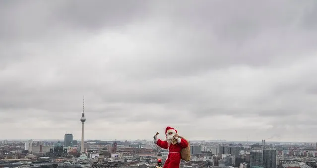 A man dressed as Father Christmas aka Santa Claus poses on the top of the Kollhoff tower in front of a Berlin skyline, on December 17, 2017 as part of a yearly stunt before the festive season. (Photo by John MacDougall/AFP Photo)