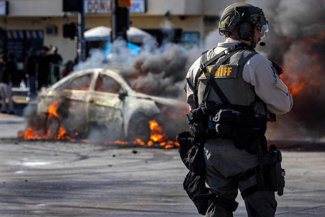 Smoke rises from a burning car on Atlantic Boulevard, during a standoff by protesters and law enforcement, following multiple detentions by Immigration and Customs Enforcement (ICE), in the Los Angeles County city of Paramount, California, on June 7, 2025. (Photo by Barbara Davidson/Reuters)