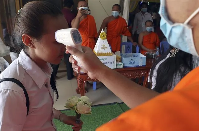 A girl, left, has her temperature checked before she offers foods during a ceremony to celebrate Pchum Ben (Ancestors' Day) at a Buddhist pagoda in Phnom Penh, Cambodia, Saturday, September 12, 2020. Cambodians celebrated their traditional 15-day Pchum Ben festival aimed at paying respect to deceased relatives. (Photo by Heng Sinith/AP Photo)