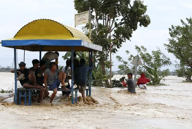 Residents take shelter under a shed as other villagers hold onto a rope to cross a flooded road amidst a strong current in Sta Rosa, Nueva Ecija in northern Philippines October 19, 2015, after it was hit by Typhoon Koppu. (Photo by Erik De Castro/Reuters)
