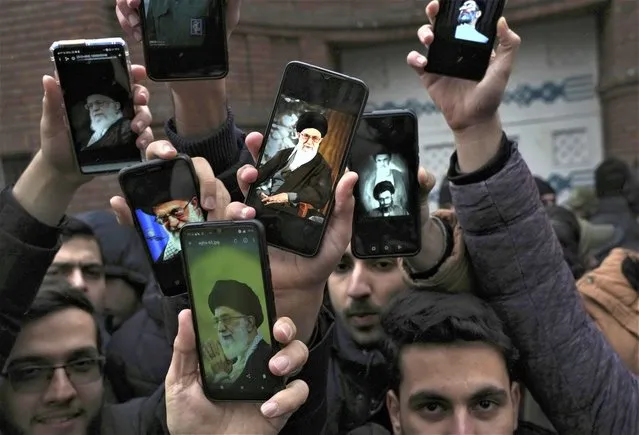 Iranian demonstrators show photos of the Supreme Leader Ayatollah Ali Khamenei on the screen of their cellphones during their protest against cartoons published by the French satirical magazine Charlie Hebdo that lampoon Iran's ruling clerics, in front of the French Embassy in Tehran, Iran, Wednesday, January 11, 2023. (Photo by Vahid Salemi/AP Photo)