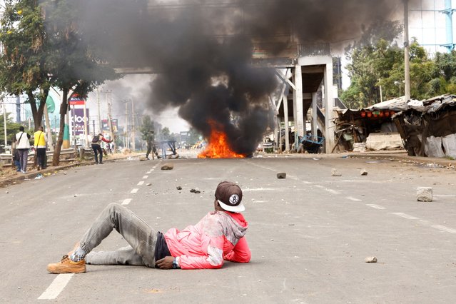 A demonstrator lies on the road, watching clashes with police as a fire burns, at the “Saba Saba People's March” anti-government protest in Nairobi, Kenya on July 7, 2025. (Photo by Thomas Mukoya/Reuters)