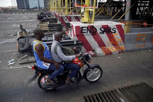 People drive past burnt toll gates with anti police slogans sprayed across, in Lagos Friday, October 23, 2020. (Photo by Sunday Alamba/AP Photo)