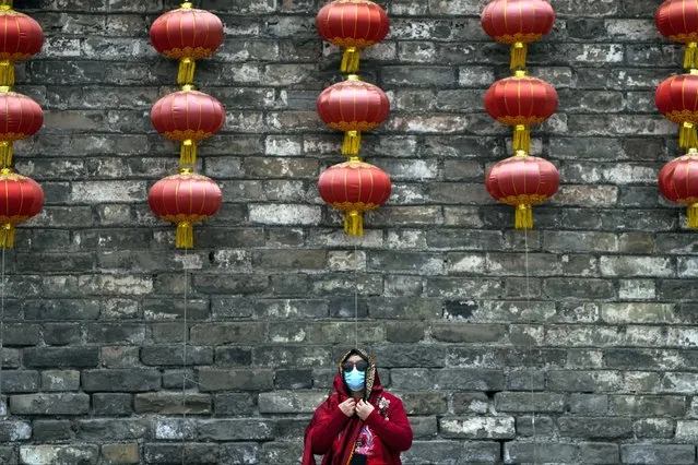 A woman wearing a face mask adjusts her scarf near a wall with lanterns on display in Beijing, Monday, April 3, 2023. (Photo by Andy Wong/AP Photo)