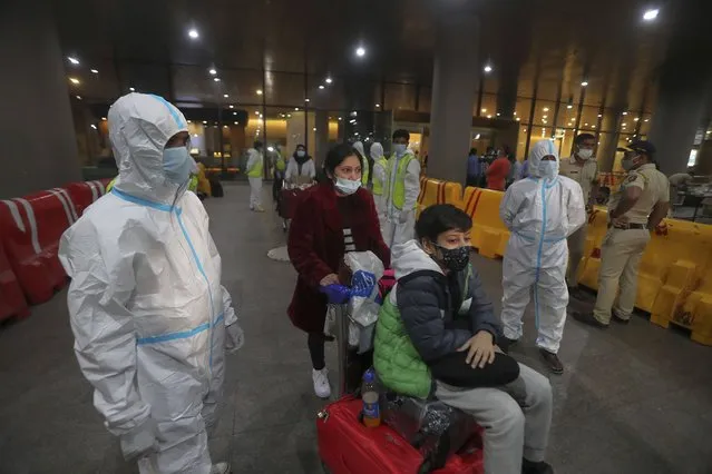 Indian municipal workers in personal protective equipment (PPE) guide passengers arriving from United Kingdom, at Chhatrapati Shivaji Maharaj International Airport in Mumbai, India, Tuesday, December 22, 2020. Dozens of countries around the world slapped tough travel restrictions on the U.K. because of a new and seemingly more contagious strain of the coronavirus in England. From Canada to India, one nation after another banned flights from Britain. (Photo by Rafiq Maqbool/AP Photo)