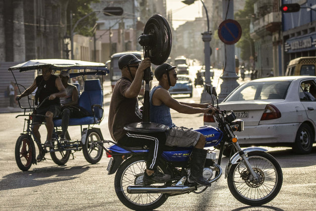 Men ride a motorcycle carrying a fan in Havana, Cuba, Thursday, April 6, 2023. As Cuban citizens deal with the country´s many problems like electricity blackouts, empty stores and long lines for almost any service, they also have to manage with the lack of public transportation as there is a shortage of working buses and few privately owned vehicles. (Photo by Ramon Espinosa/AP Photo)