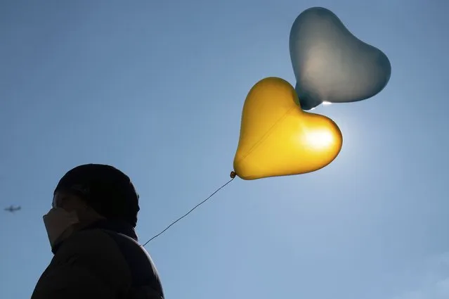A man carries balloons in the colors of Ukraine during a demonstration against the Russian attack on Ukraine, in Mainz, Germany, Sunday, March 6, 2022. (Photo by Sebastian Gollnow/dpa via AP Photo)