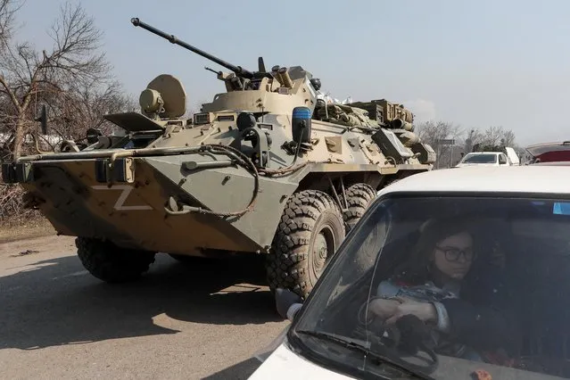 A refugee waits in a car as an armoured personnel carrier of pro-Russian troops drives out of a checkpoint in the course of Ukraine-Russia conflict in the besieged southern port city of Mariupol, Ukraine on March 24, 2022. (Photo by Alexander Ermochenko/Reuters)
